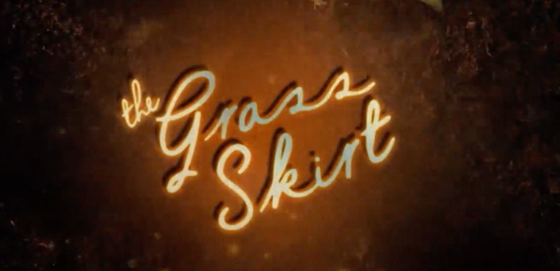 Glowing cursive text reads "the Grass Skirt" on a dark, textured background.