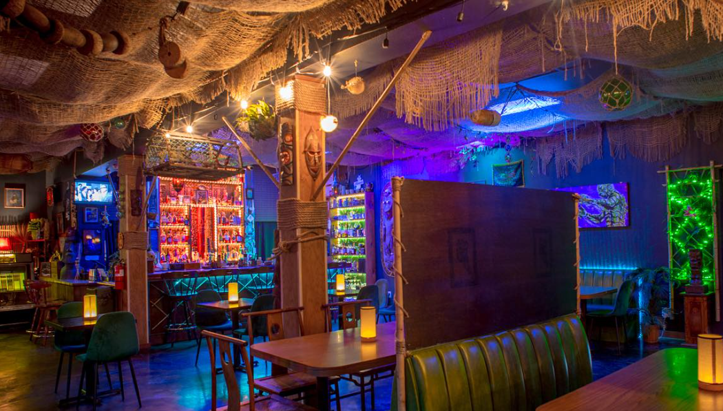 Dimly lit, colorful bar with booths and neon lights, creating a cozy, eclectic atmosphere.