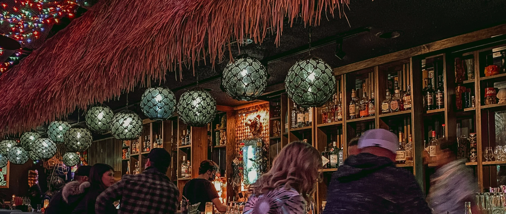 Dimly lit bar with hanging lanterns and people gathered at the counter.