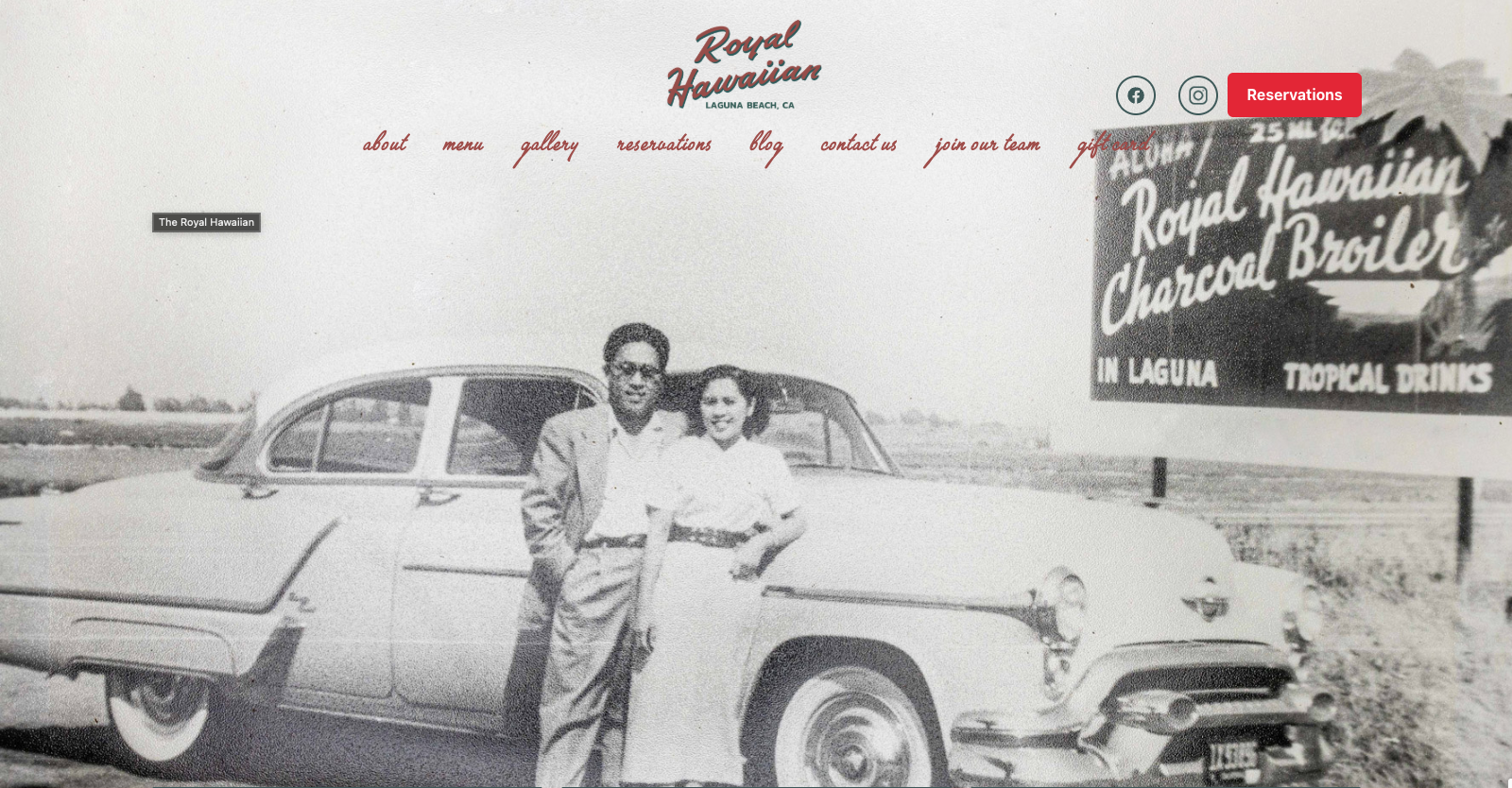 Black and white photo of a couple leaning on a vintage car next to a roadside billboard.
