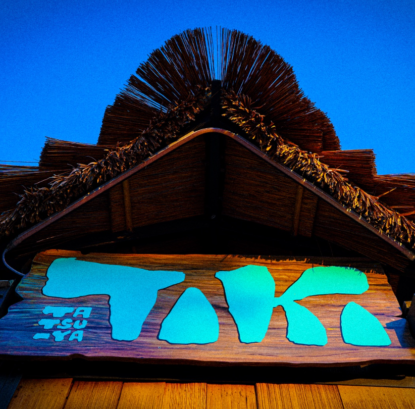 Tiki bar sign with straw roof at dusk.