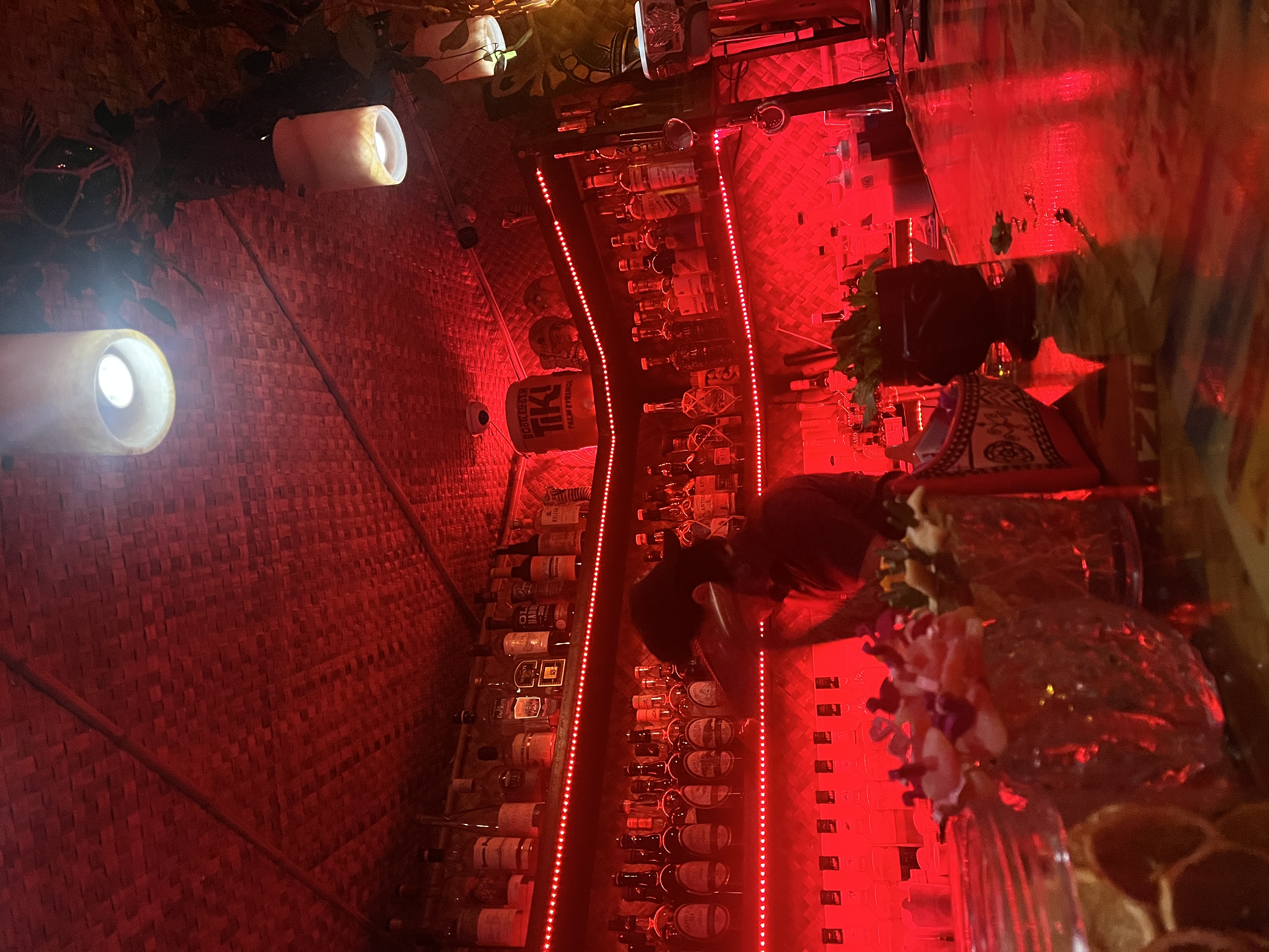 Dimly lit bar with red lights and bottles lining the shelves.