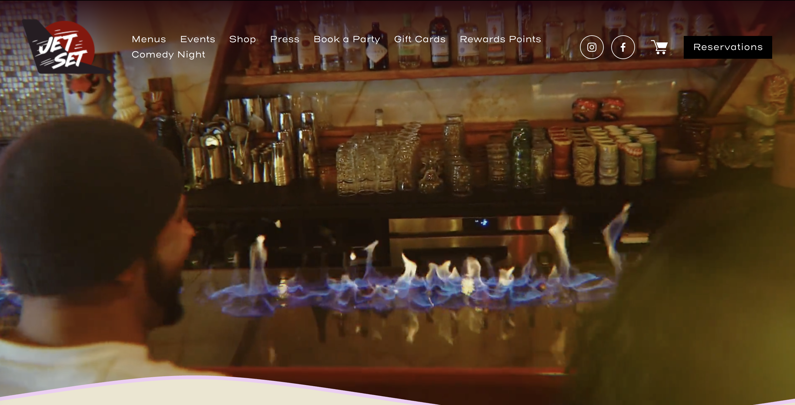 Bar with colorful lights and bottles, a person sits nearby.