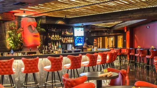 Bar with red chairs, stylish decor, and a TV behind the counter.