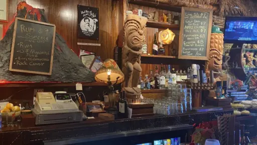 Tiki bar with carved wooden figures and retro menu boards.