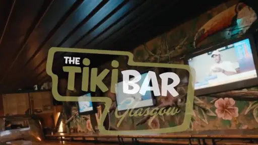 Tiki bar interior with tropical decor and wall-mounted screens.