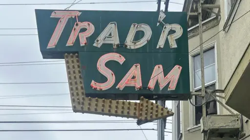 A vintage sign reads "TRADR SAM" with an arrow, against a cloudy sky.